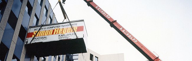Ein Kran hebt einen mit Simon Hegele beschrifteten Transportcontainer an einem Gebäude hoch