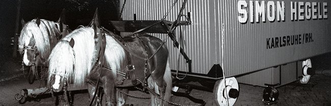 Zwei Pferde ziehen einen mit "Simon Hegele" beschrifteten Container